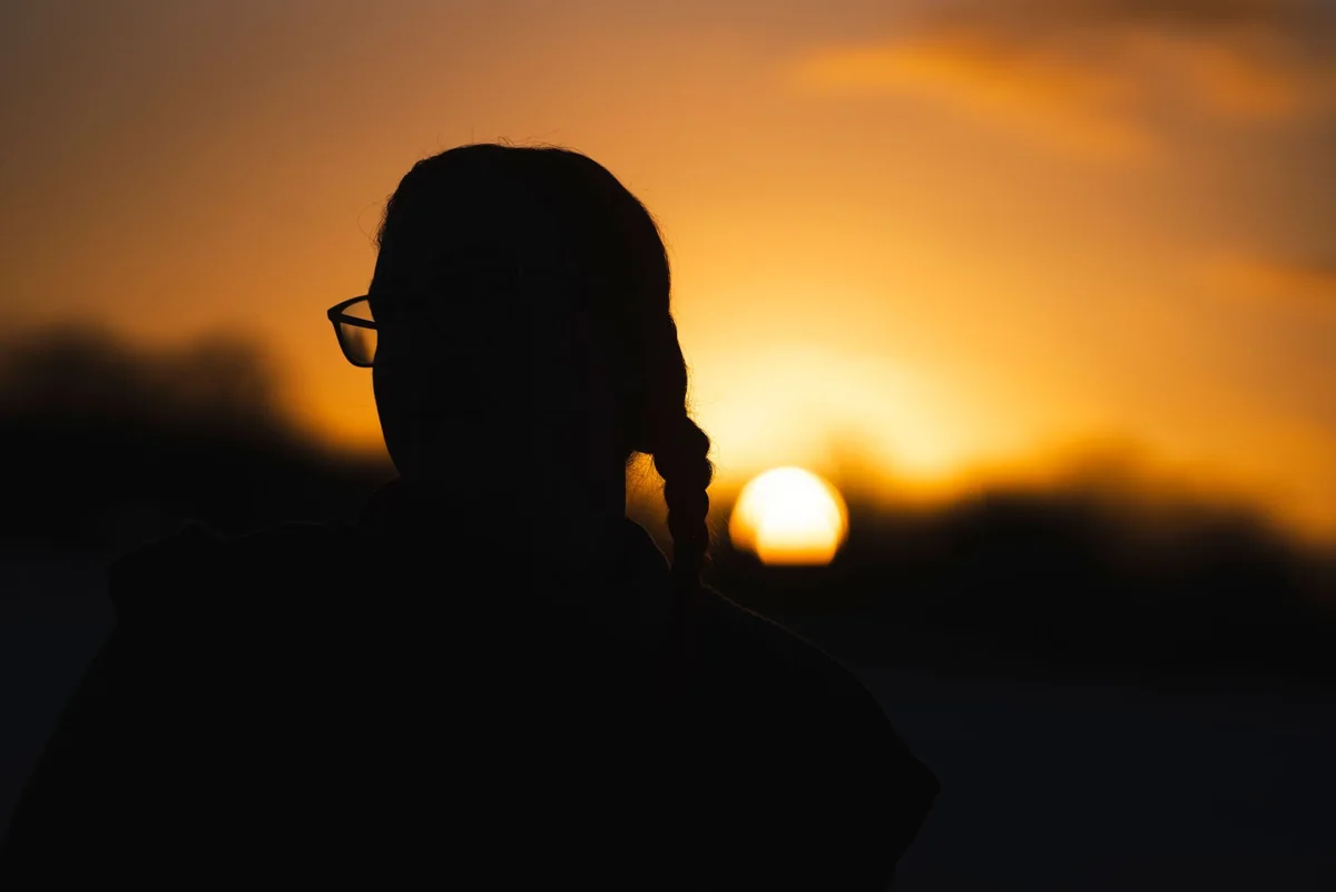 Silhouette einer Frau vor orangefarbenem Abendhimmel